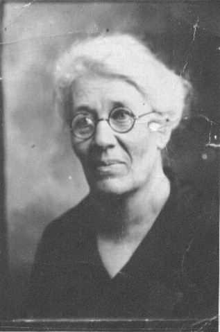 A Portrait of Nellie Hickman, smiling and wearing glasses."